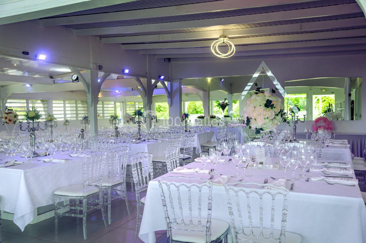 Salle de réception lumineuse avec tables dressées, chaises transparentes et décorations florales élégantes.