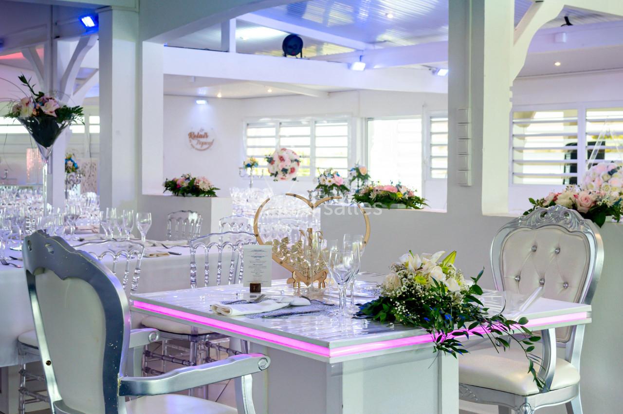 Table décorée avec des fleurs et des verres dans une salle lumineuse, avec des chaises argentées et un éclairage tamisé.
