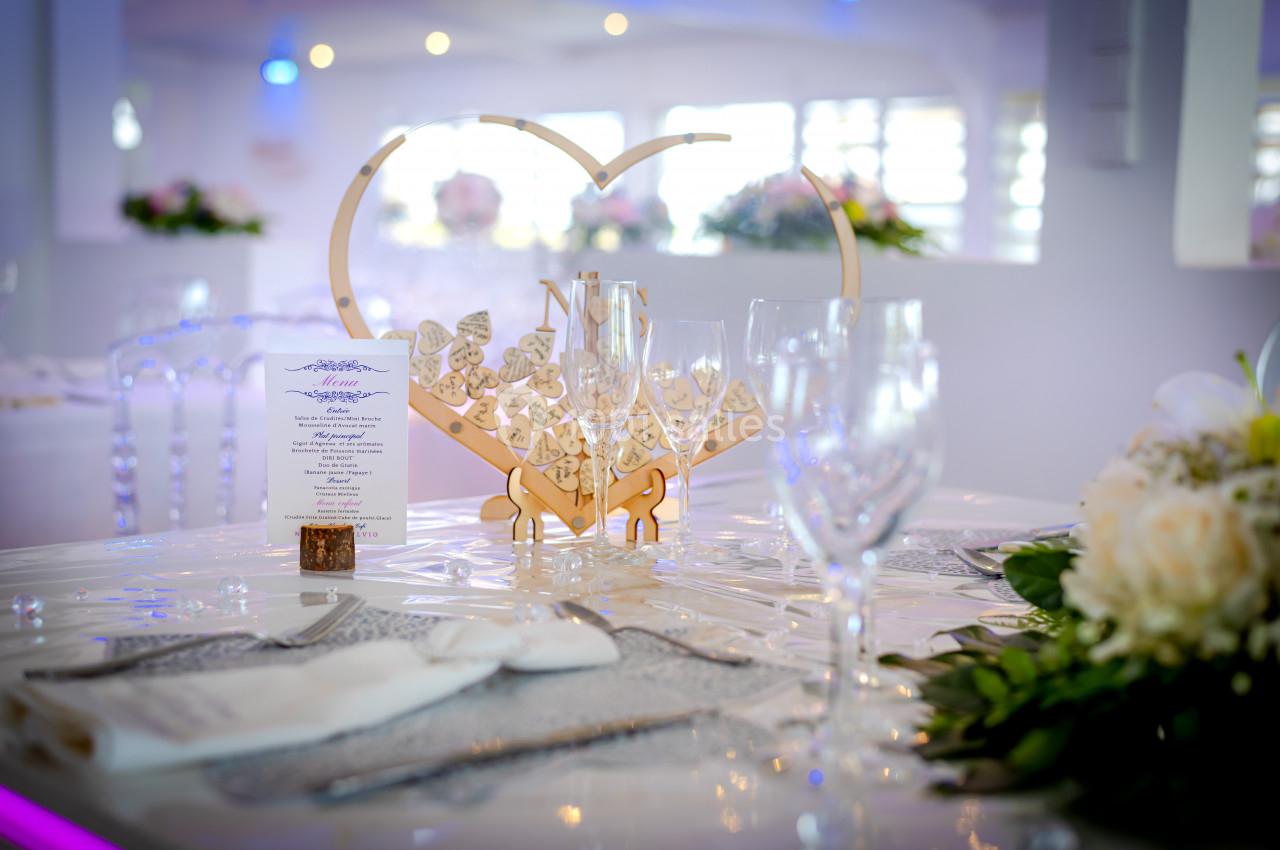 Table décorée pour un événement avec centre de table en forme de cœur, verres, menu et fleurs blanches.