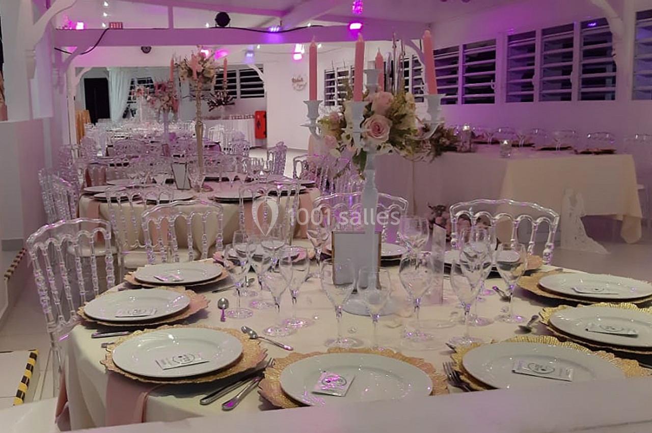 Salle de réception décorée avec des tables rondes élégantes, nappes claires, vaisselle raffinée et centres de table fleuris.