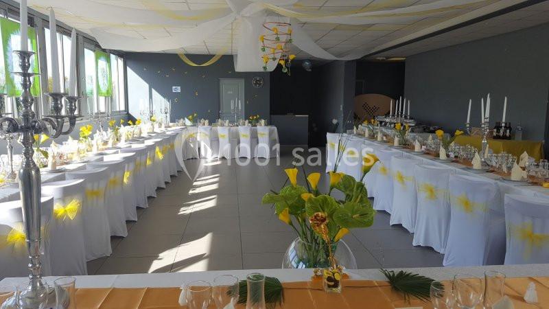 Location salle Bonneuil-sur-Marne (Val-de-Marne) - Salle des Petits Carreaux #15 Salle décorée pour un événement avec tables alignées, nappes blanches, centres de table floraux et guirlandes au plafond.