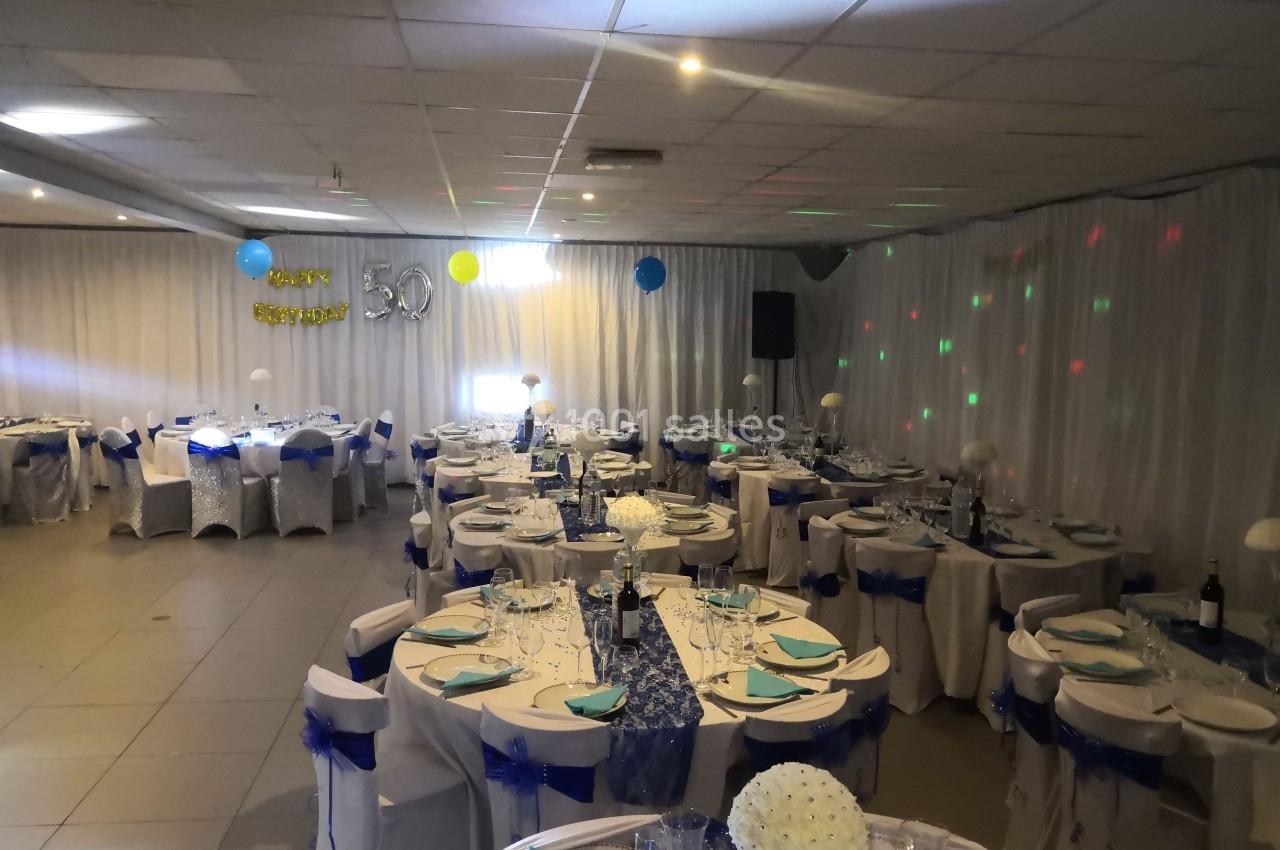 Location salle Bonneuil-sur-Marne (Val-de-Marne) - Salle des Petits Carreaux #2 Salle décorée pour une fête avec tables dressées, nappes blanches, rubans bleus et ballons suspendus.