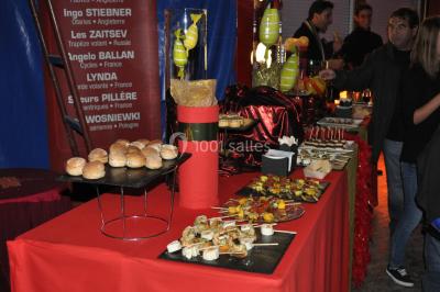 Foule faisant la queue devant un chapiteau illuminé au crépuscule, avec des montagnes en arrière-plan.