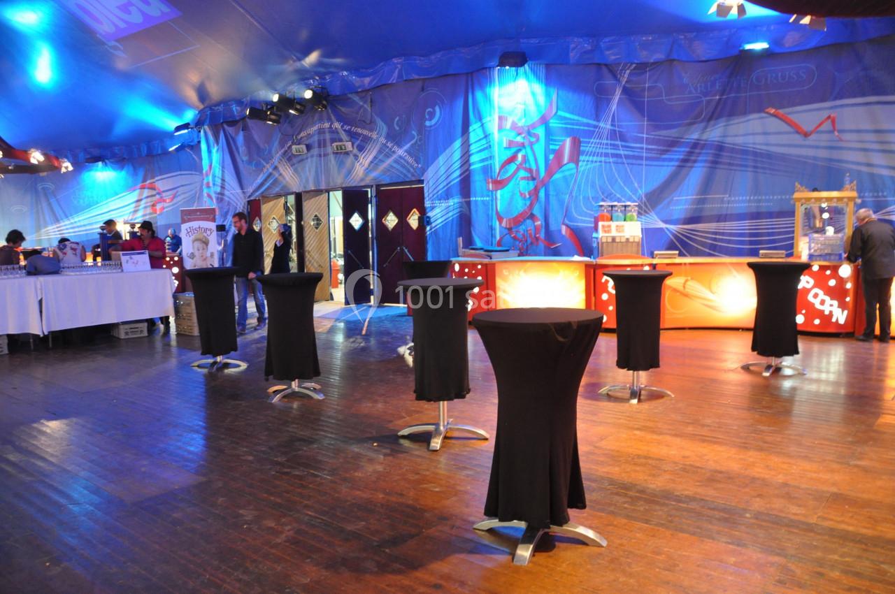 Salle de réception avec tables hautes noires, éclairage coloré et comptoirs en arrière-plan.