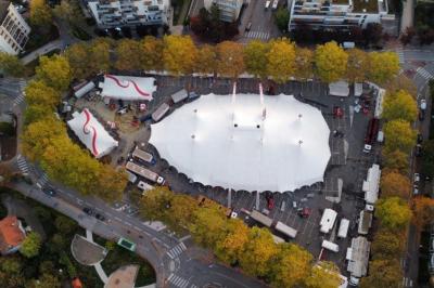 Miniature Location salle Annecy (Haute-Savoie) - Chapiteaux Arlette Gruss - Annecy #23 Vue aérienne d'un grand chapiteau blanc entouré d'arbres et de bâtiments dans un espace urbain.