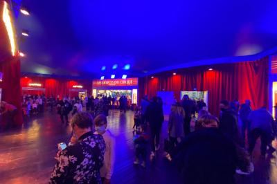 Des personnes dansent sous des éclairages colorés dans une salle sombre avec des sièges en arrière-plan.