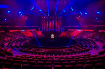 Des personnes dansent sous des éclairages colorés dans une salle sombre avec des sièges en arrière-plan.