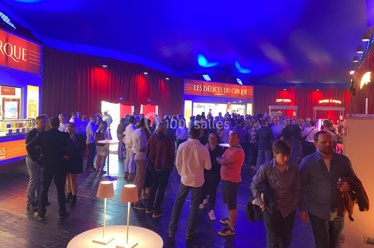 Foule rassemblée dans un chapiteau éclairé, avec des stands de restauration en arrière-plan.