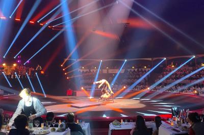 Grand chapiteau blanc et rouge installé sur un terrain gravillonné, entouré d'arbres et de structures similaires.