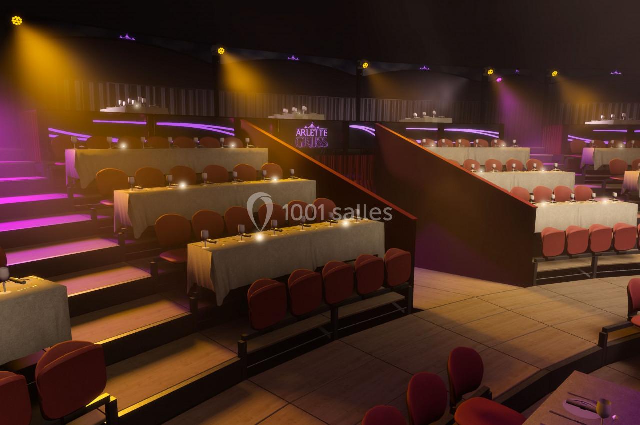 Salle de spectacle avec gradins, tables dressées et éclairage coloré créant une ambiance chaleureuse.