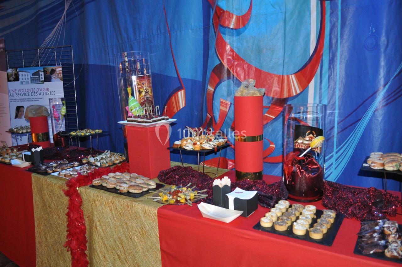 Buffet décoré avec des plats variés, des desserts et des décorations rouges sur une nappe dorée et rouge.