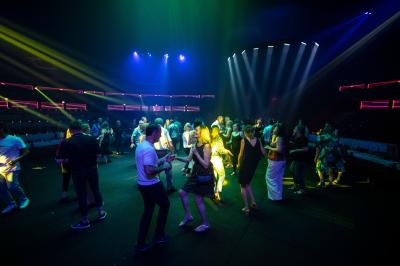 Personnes dansant sous des éclairages colorés dans une salle sombre avec des gradins en arrière-plan.