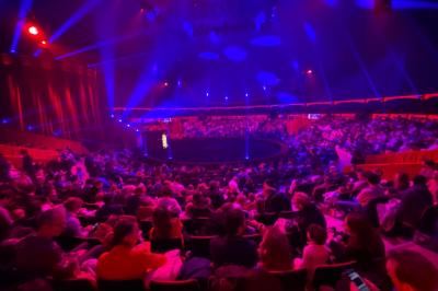 Personnes dansant sous des éclairages colorés dans une salle sombre avec des gradins en arrière-plan.