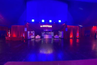 Chapiteau blanc et rouge monté sur un terrain en gravier, entouré d'arbres et de structures similaires.