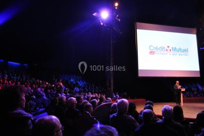 Grand chapiteau blanc et rouge installé sur un terrain gravillonné, entouré d'arbres et de structures similaires.