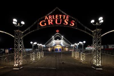 Grand chapiteau blanc et rouge monté sur un terrain en plein air, entouré d'arbres et de structures secondaires.
