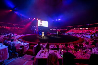 Grand chapiteau blanc et rouge monté sur un terrain en plein air, entouré d'arbres et de structures secondaires.