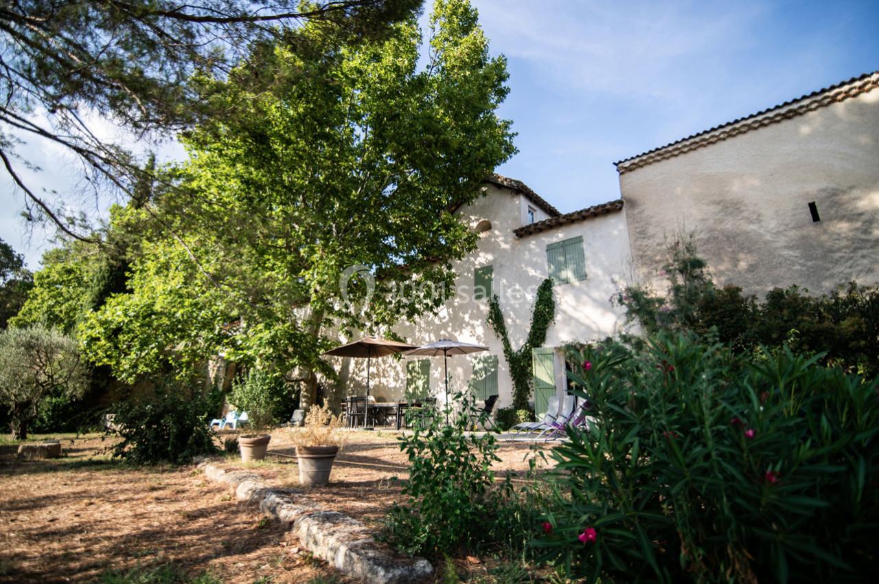 Façade d'une maison provençale entourée de végétation, avec une terrasse ombragée et des pots de fleurs.