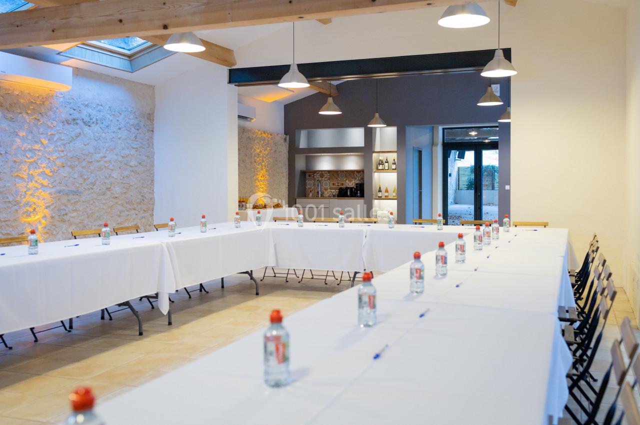Salle de réunion lumineuse avec tables disposées en U, bouteilles d'eau et stylos, éclairée par des lampes suspendues.