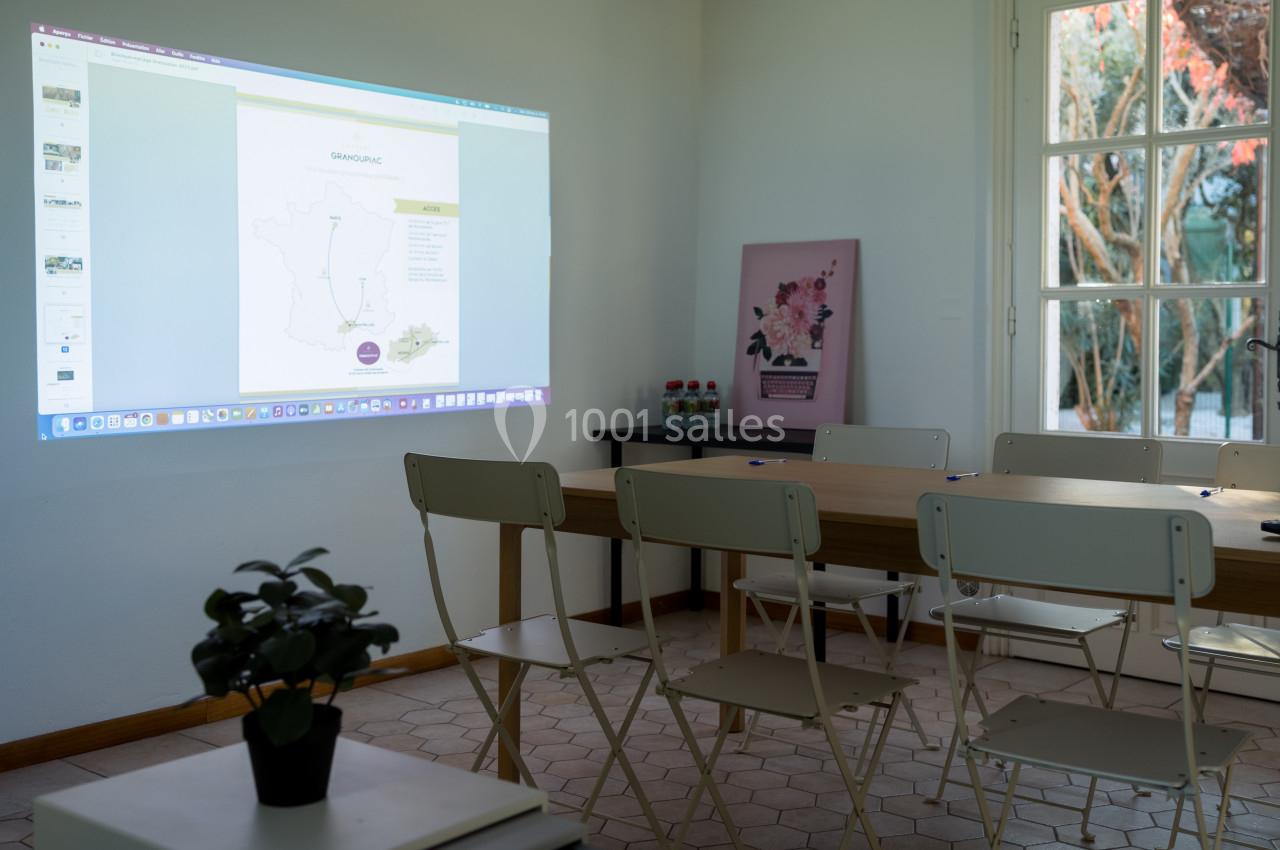 Salle de réunion lumineuse avec des chaises blanches, une table en bois et une présentation projetée au mur.