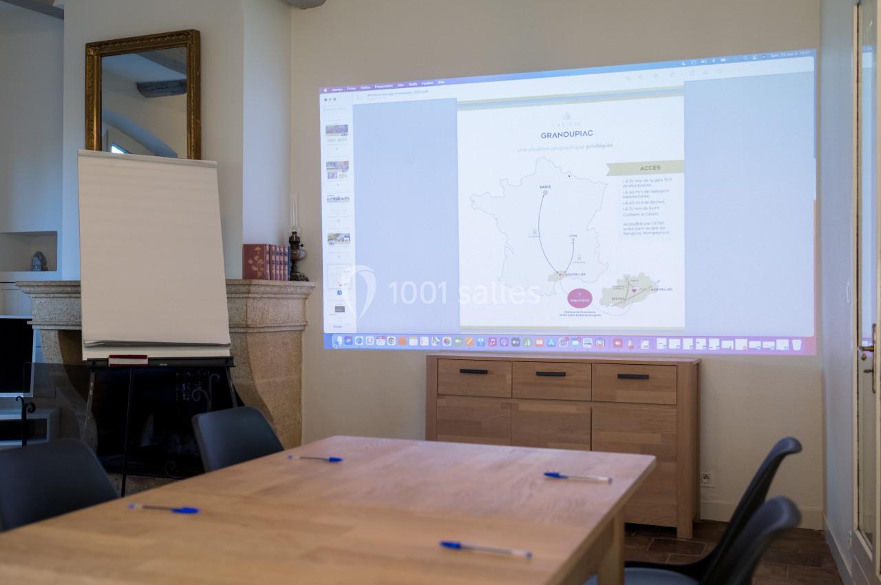 Salle de réunion avec un projecteur affichant une carte de France, un tableau blanc et une table équipée de stylos.
