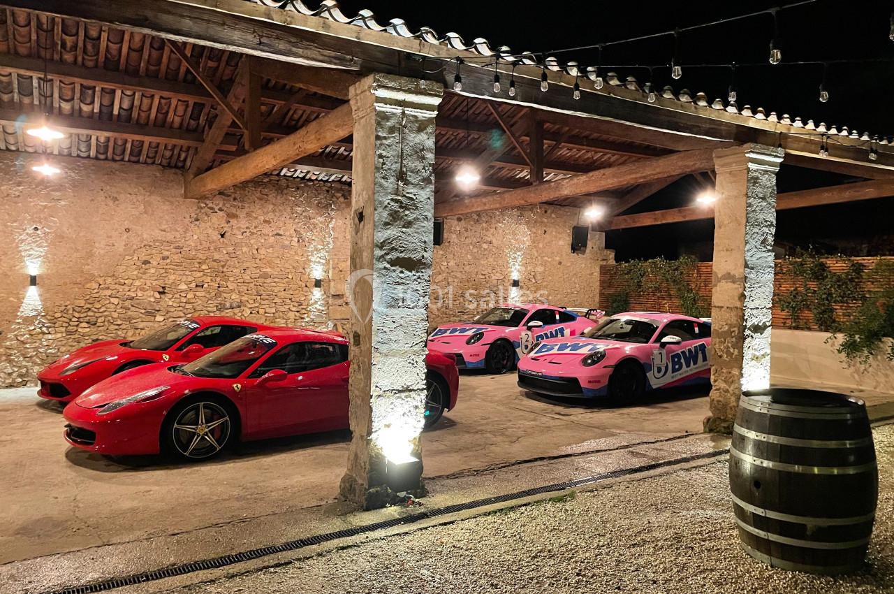 Quatre voitures de sport, deux rouges et deux roses, stationnées dans un garage en pierre éclairé la nuit.