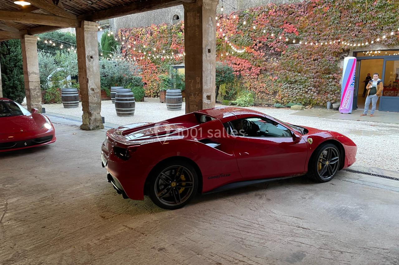 Voiture de sport rouge garée sous un auvent, avec un mur couvert de végétation en arrière-plan.