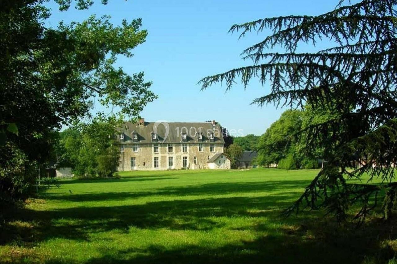 Manoir en pierre entouré d'une pelouse verdoyante et d'arbres sous un ciel bleu clair.