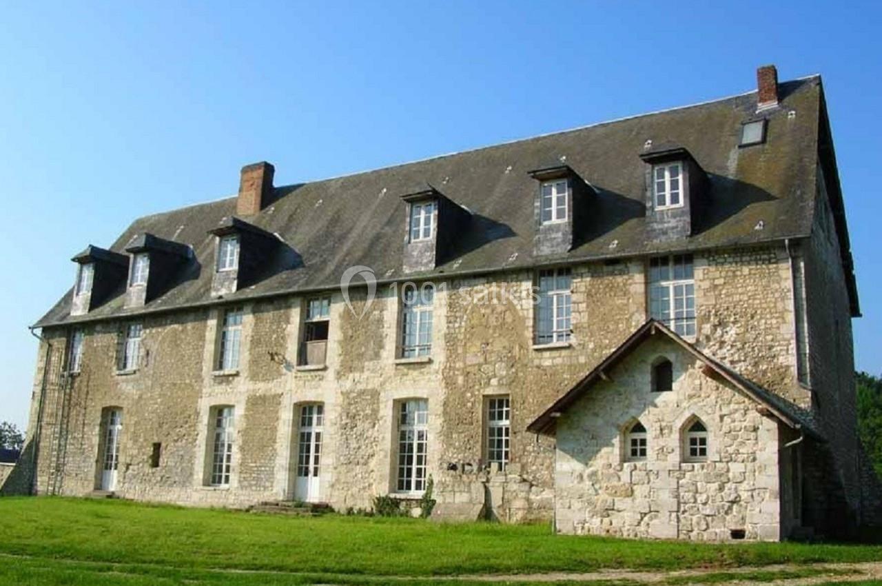 Bâtiment ancien en pierre avec toit en ardoise, plusieurs fenêtres et une petite annexe sur un terrain herbeux.