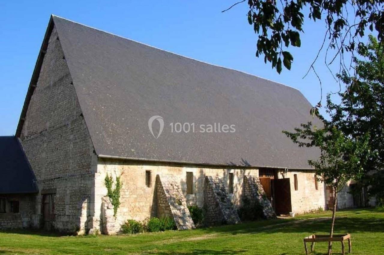 Grande grange en pierre avec un toit en ardoise, entourée de pelouse et d'arbres sous un ciel dégagé.