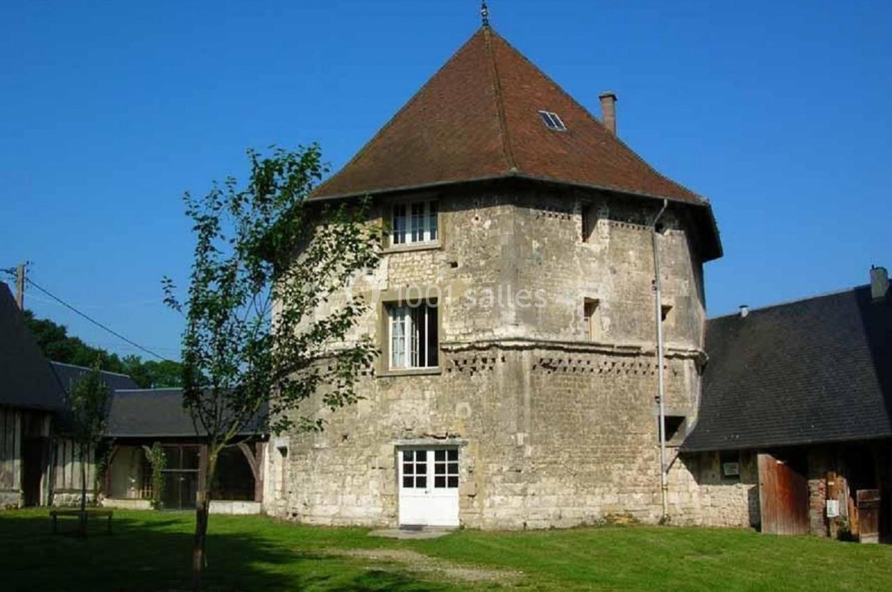 Bâtiment en pierre à toit pentagonal entouré de pelouse et d'arbres, avec des annexes en arrière-plan.