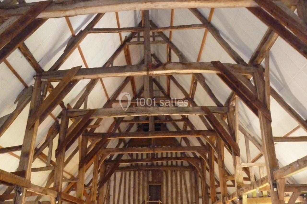 Charpente en bois apparente d'une grande salle avec murs en pierre et éclairage mural discret.