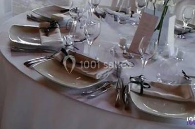 Salle de réception avec tables dressées, nappes blanches, chaises décorées et éclairage naturel à travers de grandes…