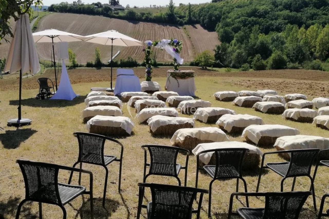 Chaises et bottes de paille disposées en extérieur pour une cérémonie, avec vue sur des champs et des collines verdoyantes.