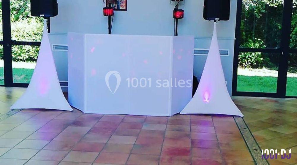 Console de DJ blanche avec éclairage coloré, entourée de deux enceintes sur pied dans une salle lumineuse.