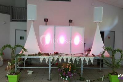 Salle de réception avec tables dressées, nappes blanches, chaises décorées et éclairage naturel à travers de grandes…