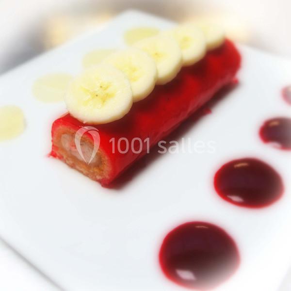 Traiteur Forest-sur-Marque (Nord) - Auberge du Tilleul #33 Dessert roulé recouvert de glaçage rouge, garni de rondelles de banane, avec des touches de coulis sur l'assiette blanche.