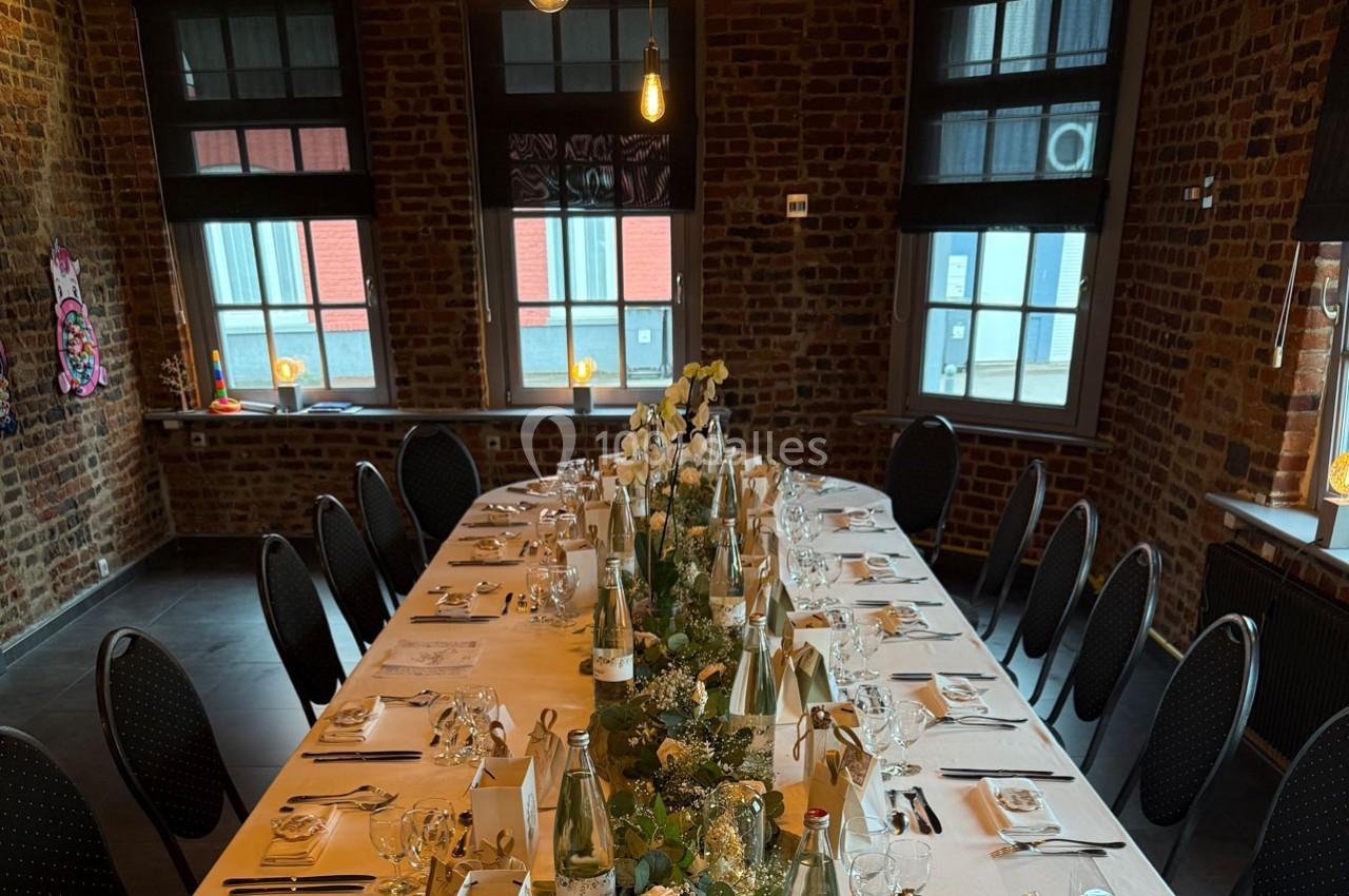 Traiteur Forest-sur-Marque (Nord) - Auberge du Tilleul #13 Table élégamment dressée pour un repas, décorée de fleurs et de bouteilles, dans une salle en briques avec grandes fenêtres.
