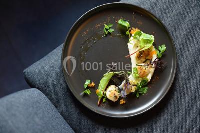 Dessert roulé recouvert de glaçage rouge, garni de rondelles de banane, avec des touches de coulis sur l'assiette blanche.