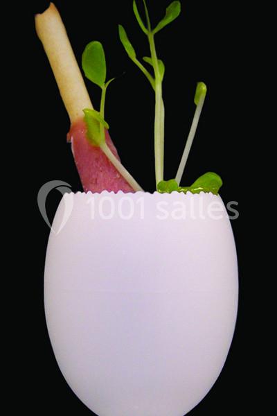 Branche de plante et bâtonnet enroulé de viande dans une coquille d'œuf blanche sur fond noir.