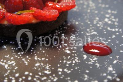 Dessert roulé recouvert de glaçage rouge, garni de rondelles de banane, avec des touches de coulis sur l'assiette blanche.