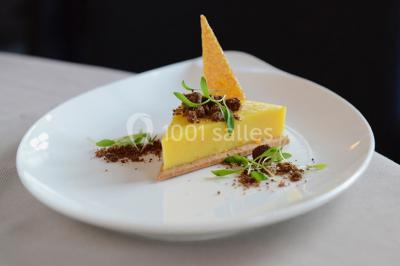 Dessert roulé recouvert de glaçage rouge, garni de rondelles de banane, avec des touches de coulis sur l'assiette blanche.