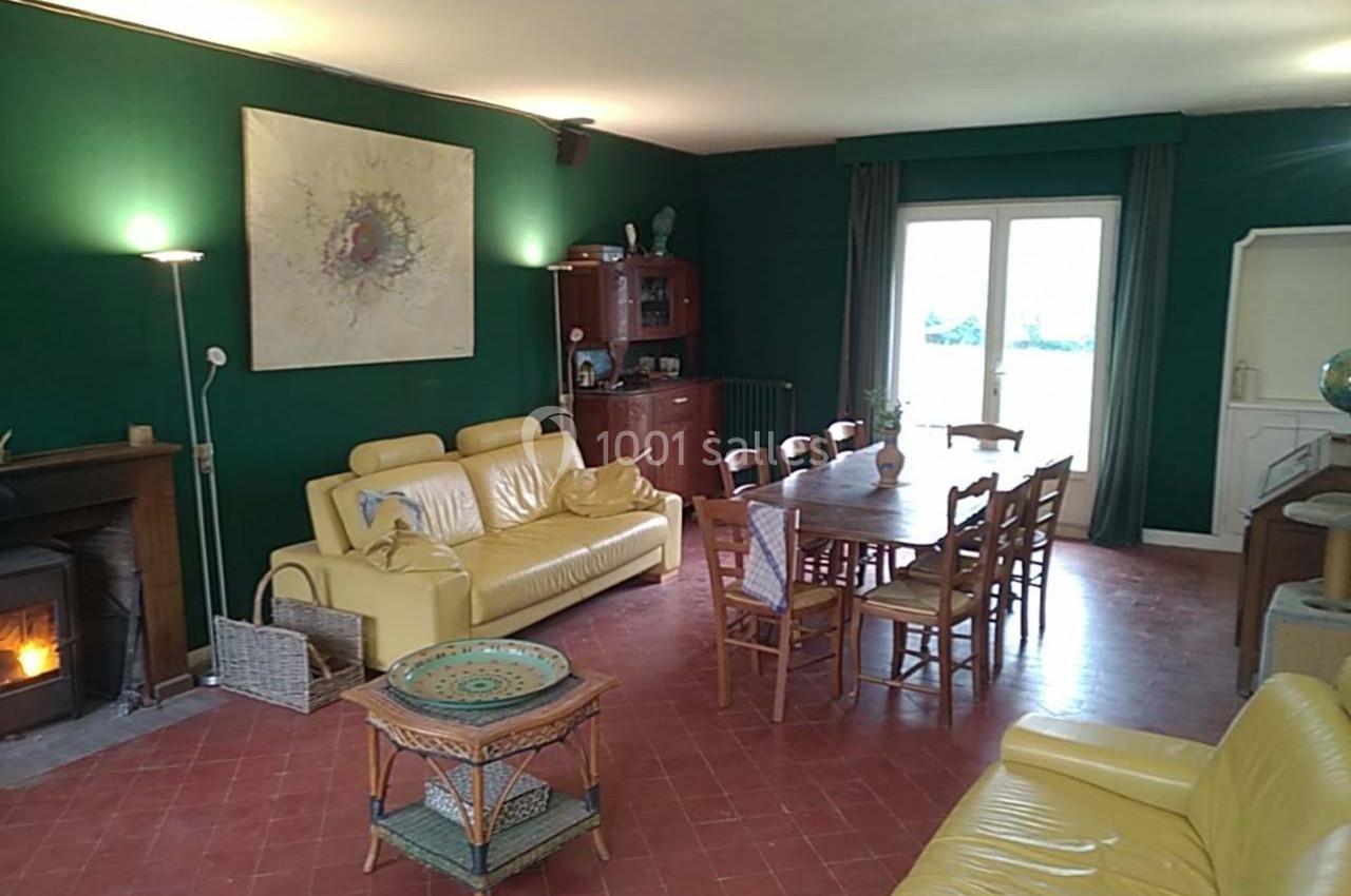 Salon avec murs verts, canapés jaunes, table en bois entourée de chaises, poêle à bois et grande fenêtre donnant sur l…