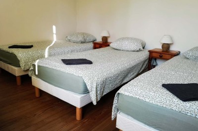 Chambre mansardée avec deux lits simples, un bureau en bois, une chaise blanche et une fenêtre de toit.