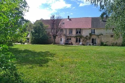 Chambre mansardée avec deux lits simples, un bureau en bois, une chaise blanche et une fenêtre de toit.