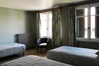 Chambre mansardée avec deux lits simples, un bureau en bois, une chaise blanche et une fenêtre de toit.