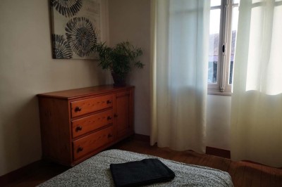 Chambre mansardée avec deux lits simples, un bureau en bois, une chaise blanche et une fenêtre de toit.