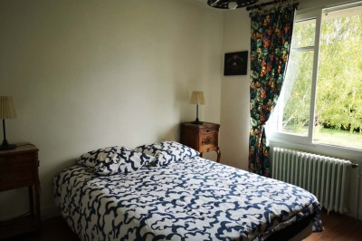 Chambre mansardée avec deux lits simples, un bureau en bois, une chaise blanche et une fenêtre de toit.