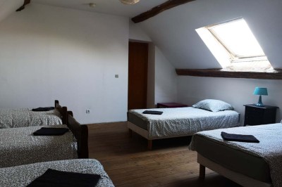 Chambre mansardée avec deux lits simples, un bureau en bois, une chaise blanche et une fenêtre de toit.