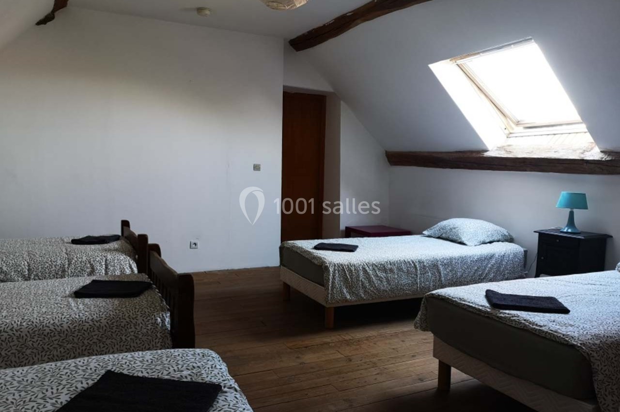 Chambre mansardée avec quatre lits simples, parquet en bois, fenêtre de toit et mobilier minimaliste.